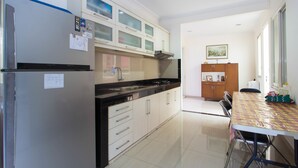 A modern kitchen with a refrigerator, stove, and cabinets. There is a dining table with chairs and a window in the background. - RedDoorz Plus near Siloam Karawaci (Curug)