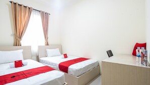 A hotel room with two beds, each with a red blanket and pillow, a desk with a chair, and a window with curtains. - RedDoorz Plus near Siloam Karawaci (Curug)