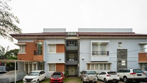 A modern two-story residential building with a central entrance, multiple balconies, and a covered parking area with several cars. - RedDoorz Plus near Siloam Karawaci (Curug)