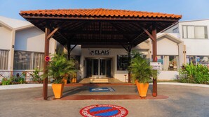 A hotel entrance with a covered patio, palm trees, and a sign for 'ELAIS POINTE- NOIRE.' - Hotel Elais (Pointe-Noire)