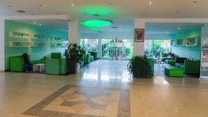 A spacious lobby with green seating areas, a central plant, and a large window providing a view of the outdoors. - Hotel Elais (Pointe-Noire)