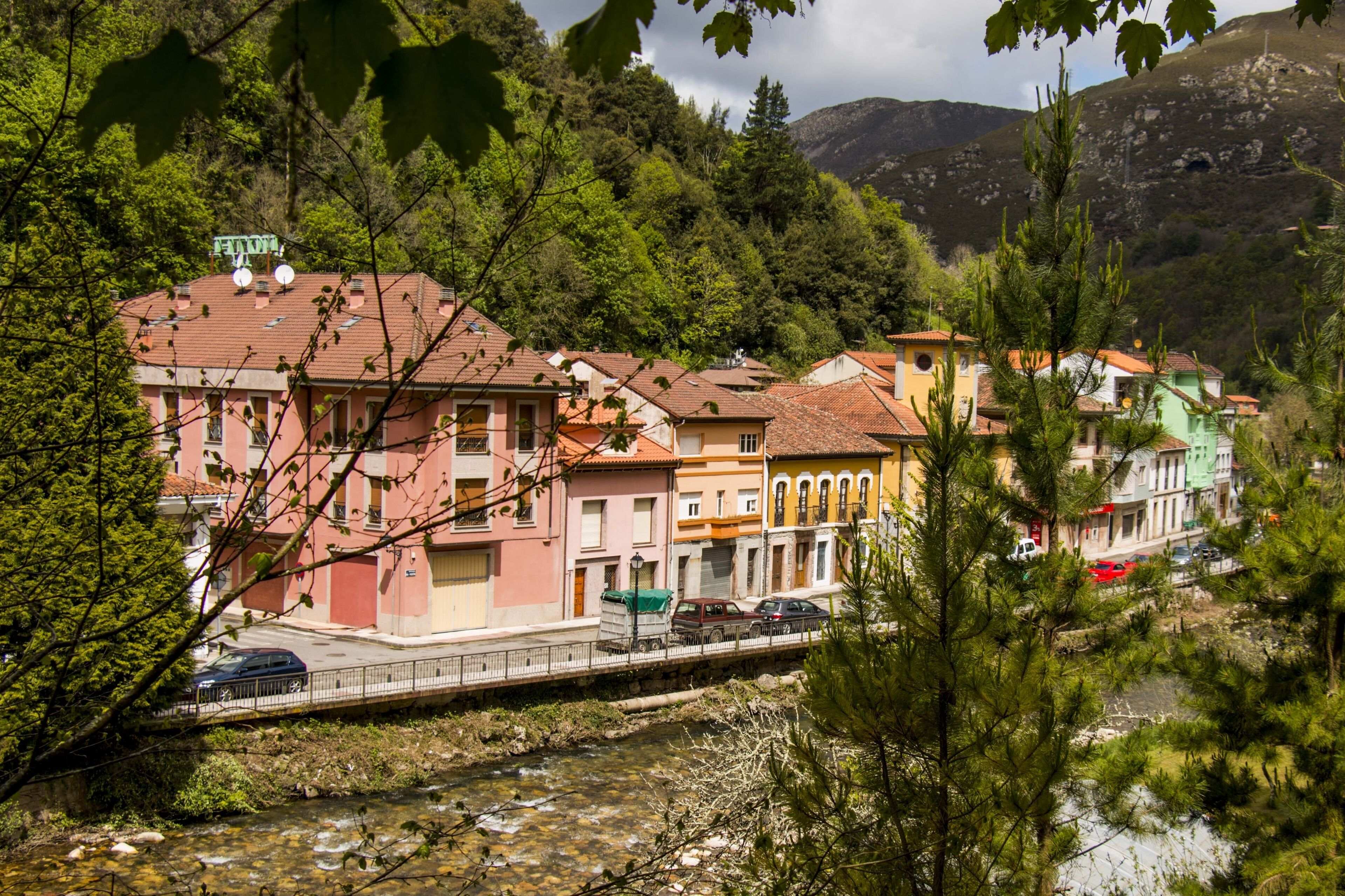 Un pueblo a orillas del río con edificios de colores, un puente y una montaña al fondo.