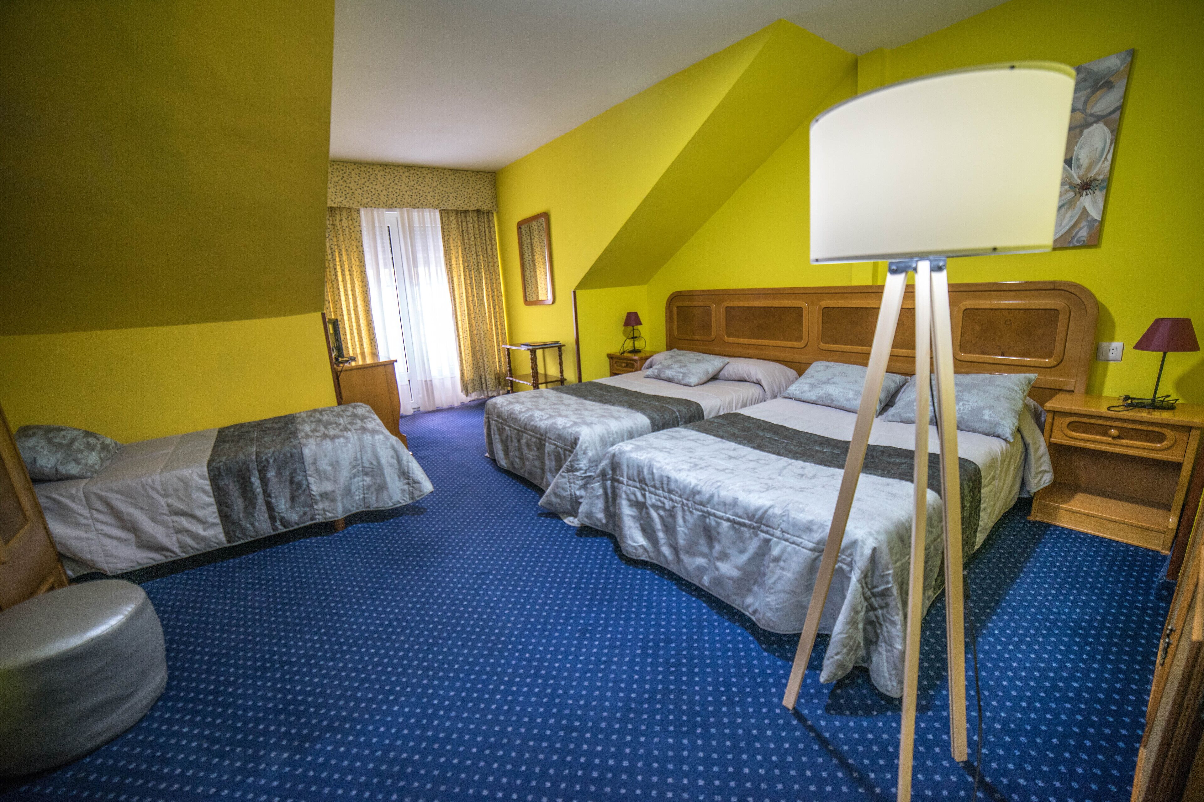 A hotel room with two single beds, a large bed, a standing easel, a desk, and a chair.