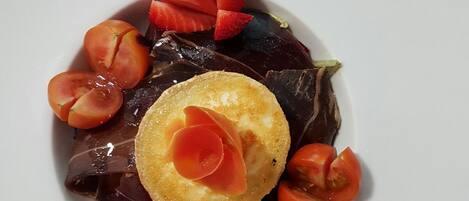 Un plato blanco con un alimento de color oscuro, adornado con fresas y un detalle decorativo, bañado en salsa de chocolate.