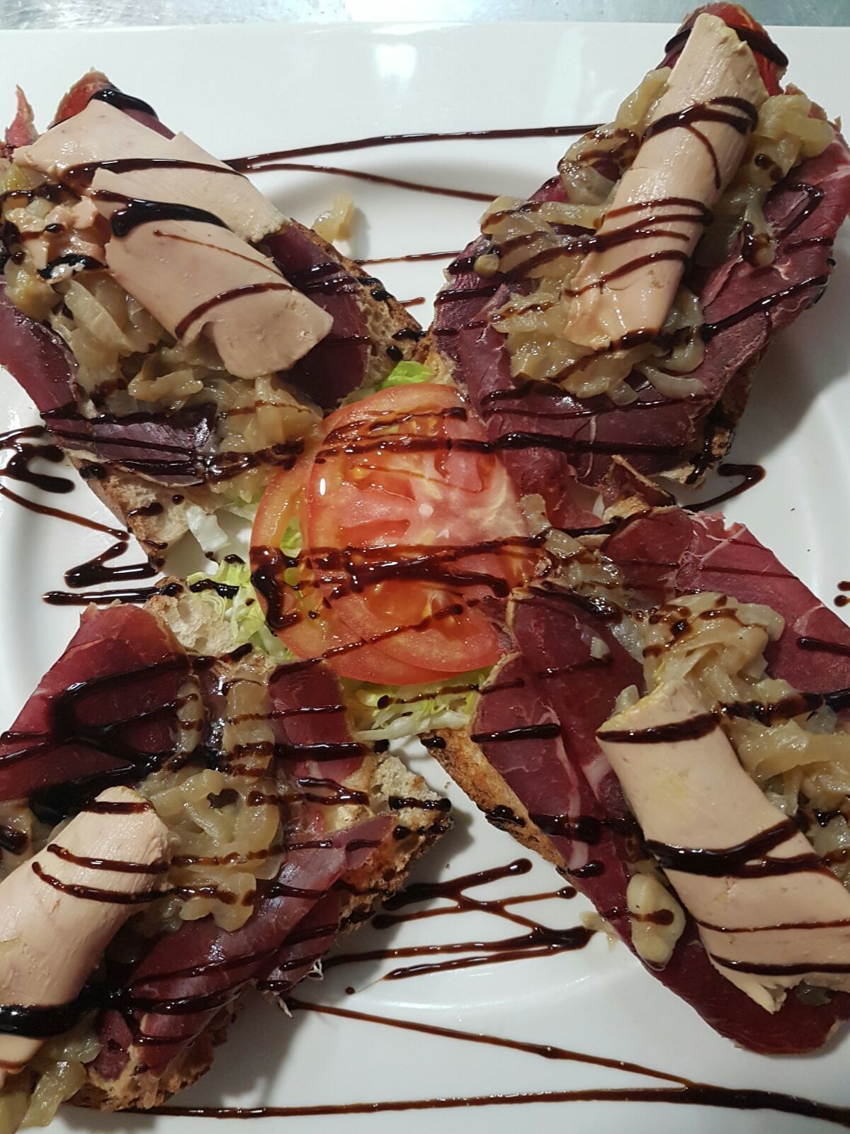 A dish with a central tomato slice surrounded by various ingredients and drizzled with sauce.