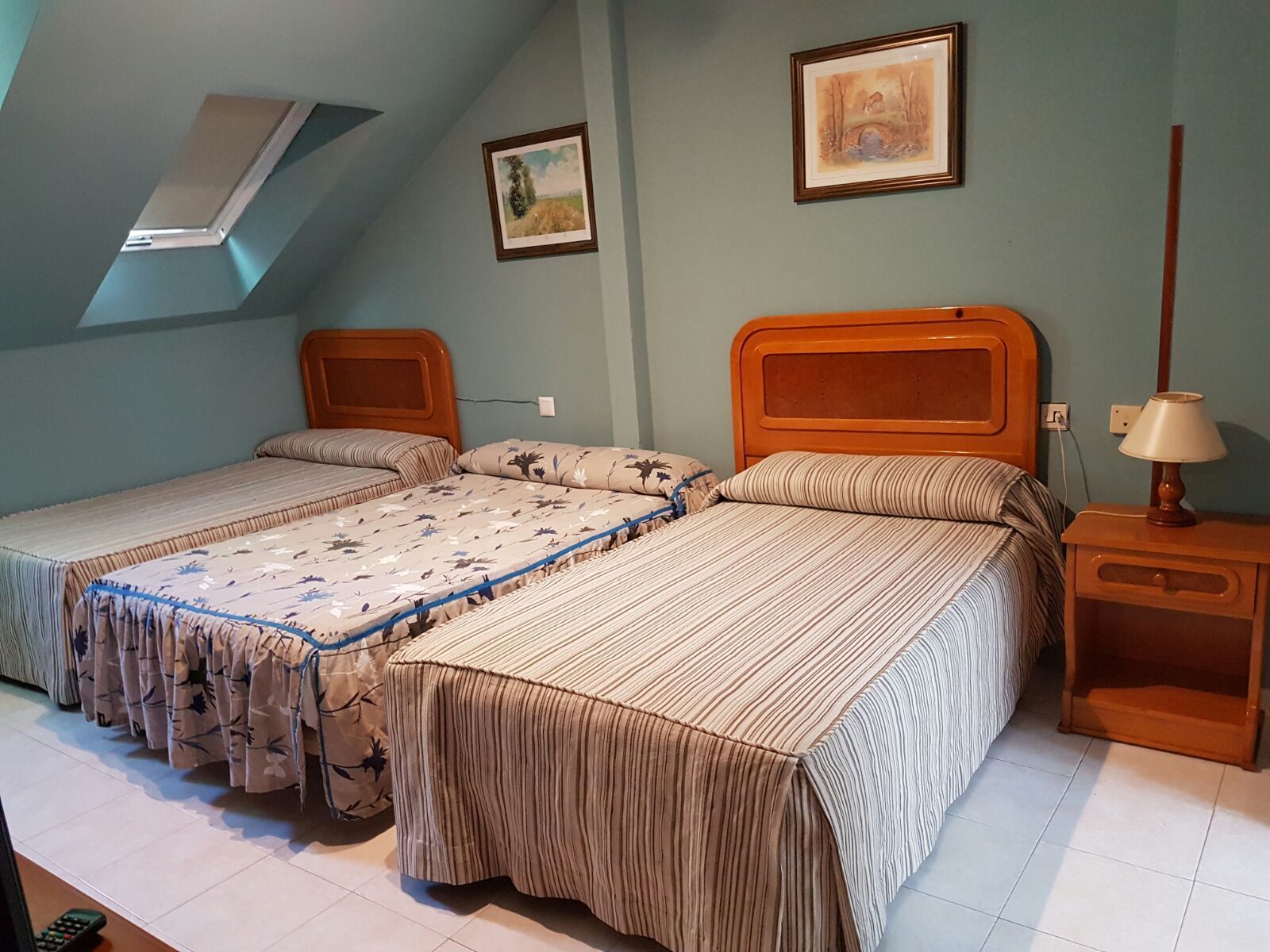 Un dormitorio con dos camas individuales, una mesita de noche con lámpara y una rejilla de ventilación en el techo.