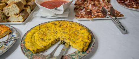 A table with various food items including bread, a bowl of red sauce, a plate of cured meat, and a slice of quiche.