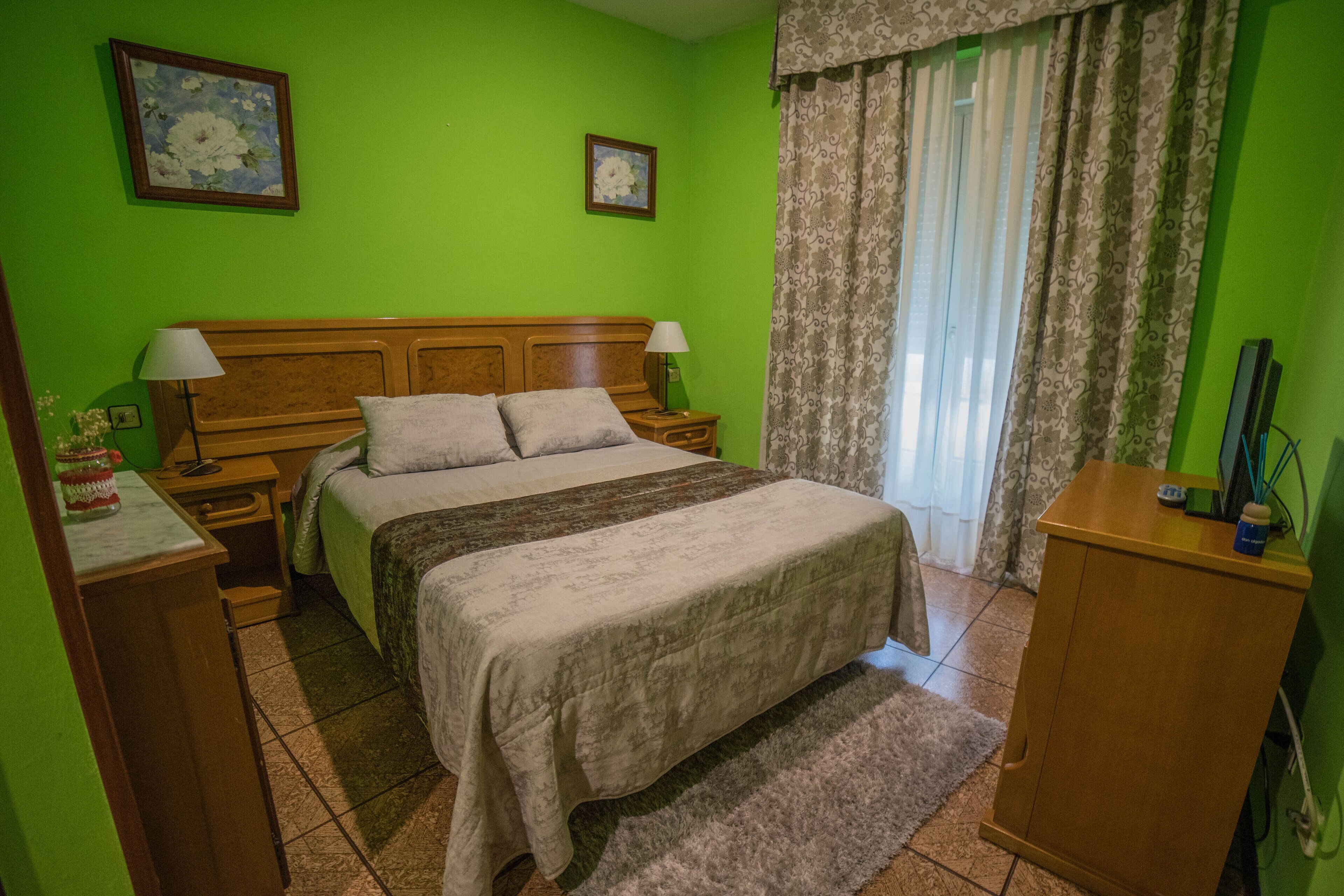 Un dormitorio con cama, mesitas de noche, cómoda y ventana con cortinas.