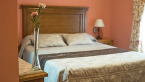 Een slaapkamer met twee bedden, een nachtkastje met een lamp en een vaas met bloemen op het nachtkastje.