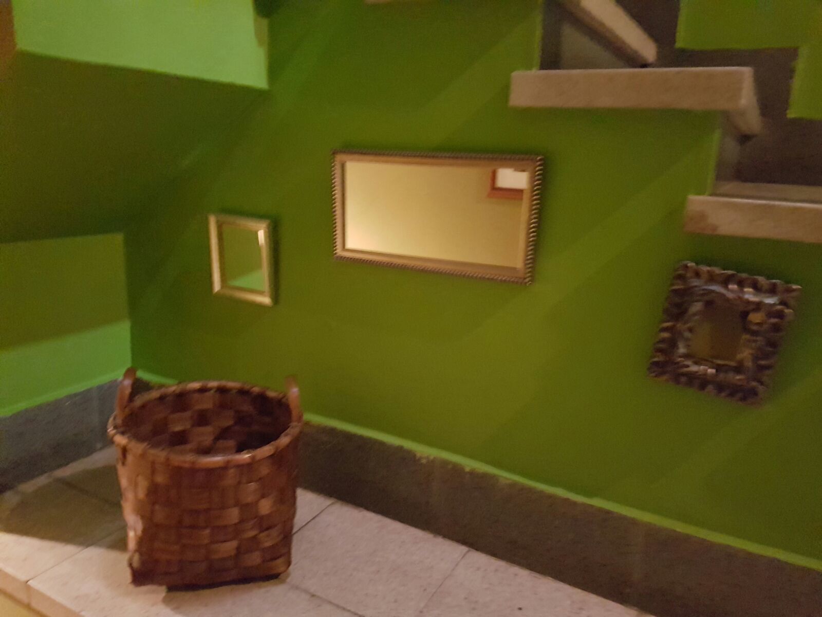 Una escalera con paredes verdes y una cesta tejida en el suelo.