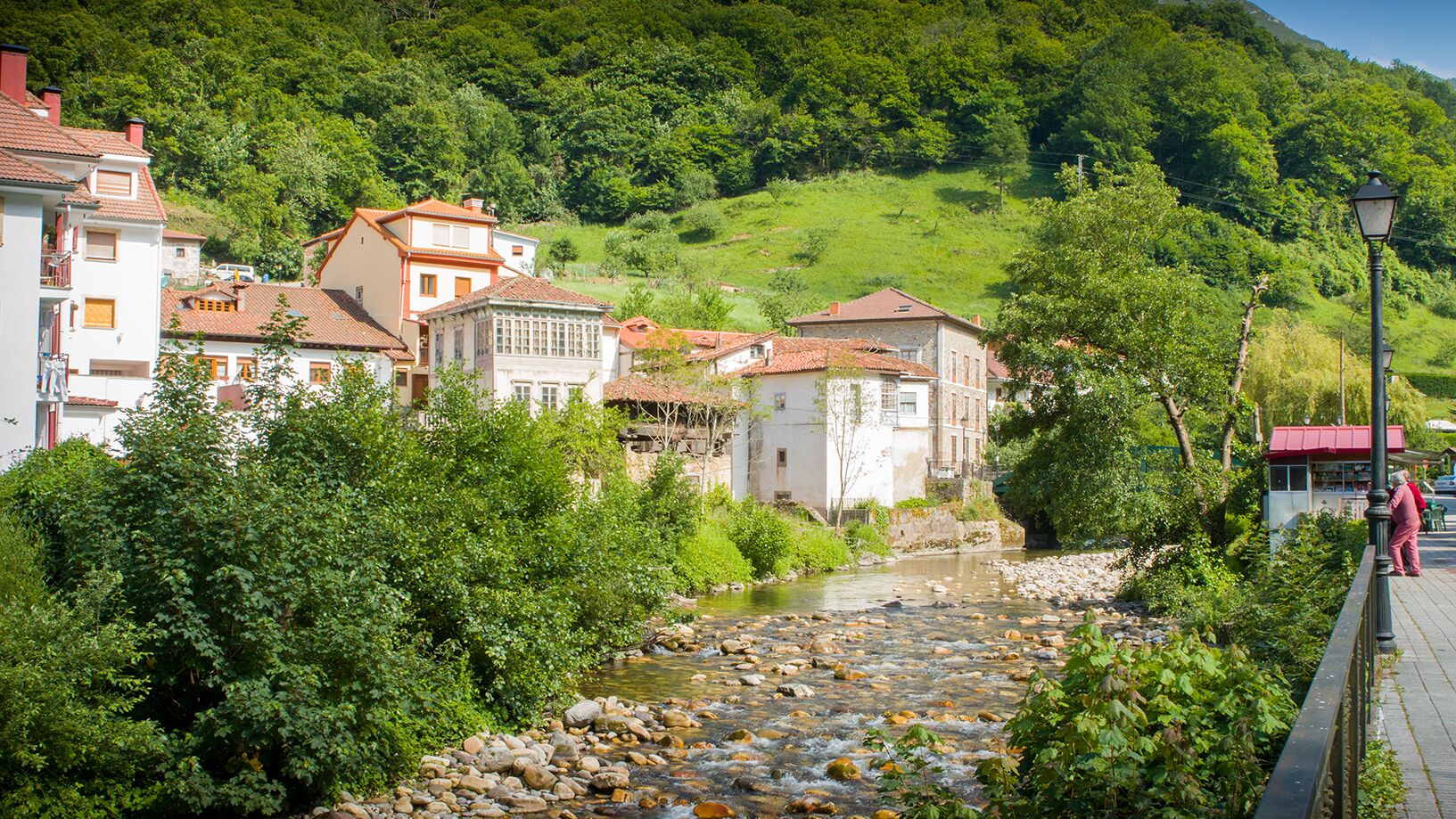 A riverside town with buildings, a pedestrian path, and a person walking.