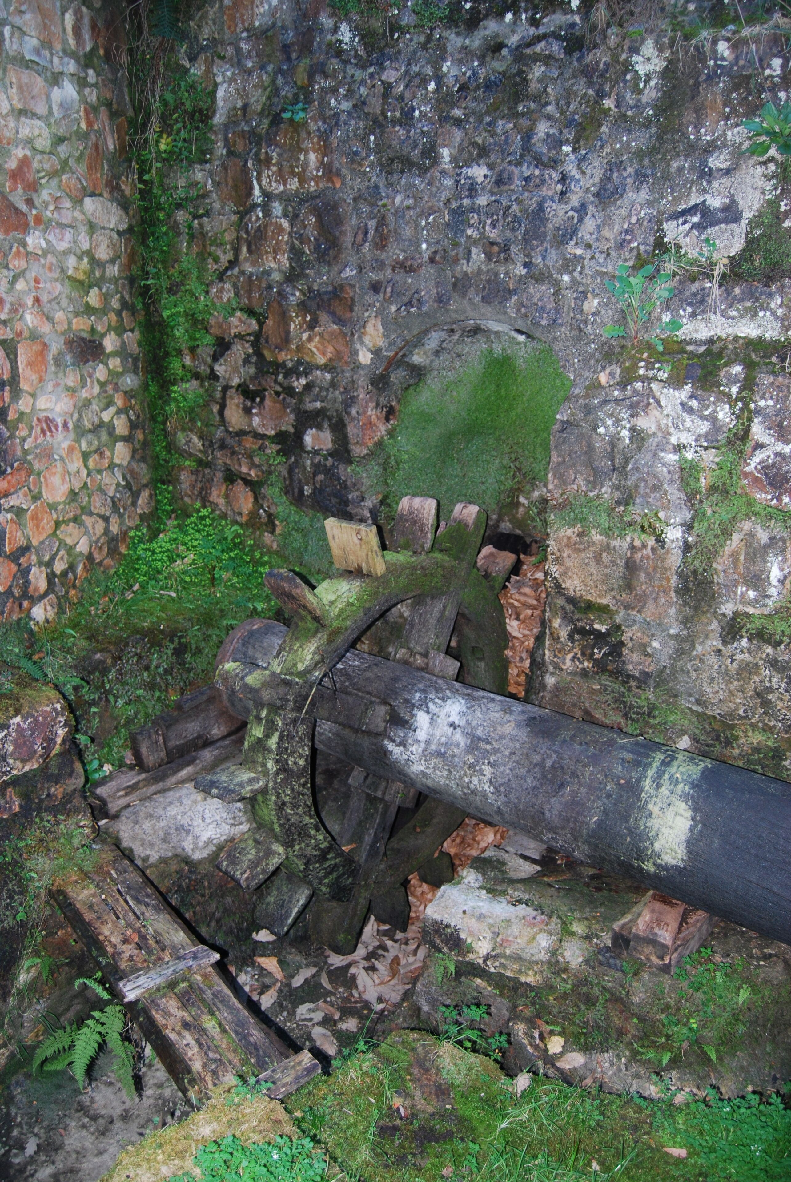 Una pared de piedra cubierta de musgo y un tubo de metal grande y oxidado.
