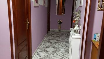 A hallway with patterned floor tiles, a wooden door, and a white cabinet with a mirror and a vase of flowers.