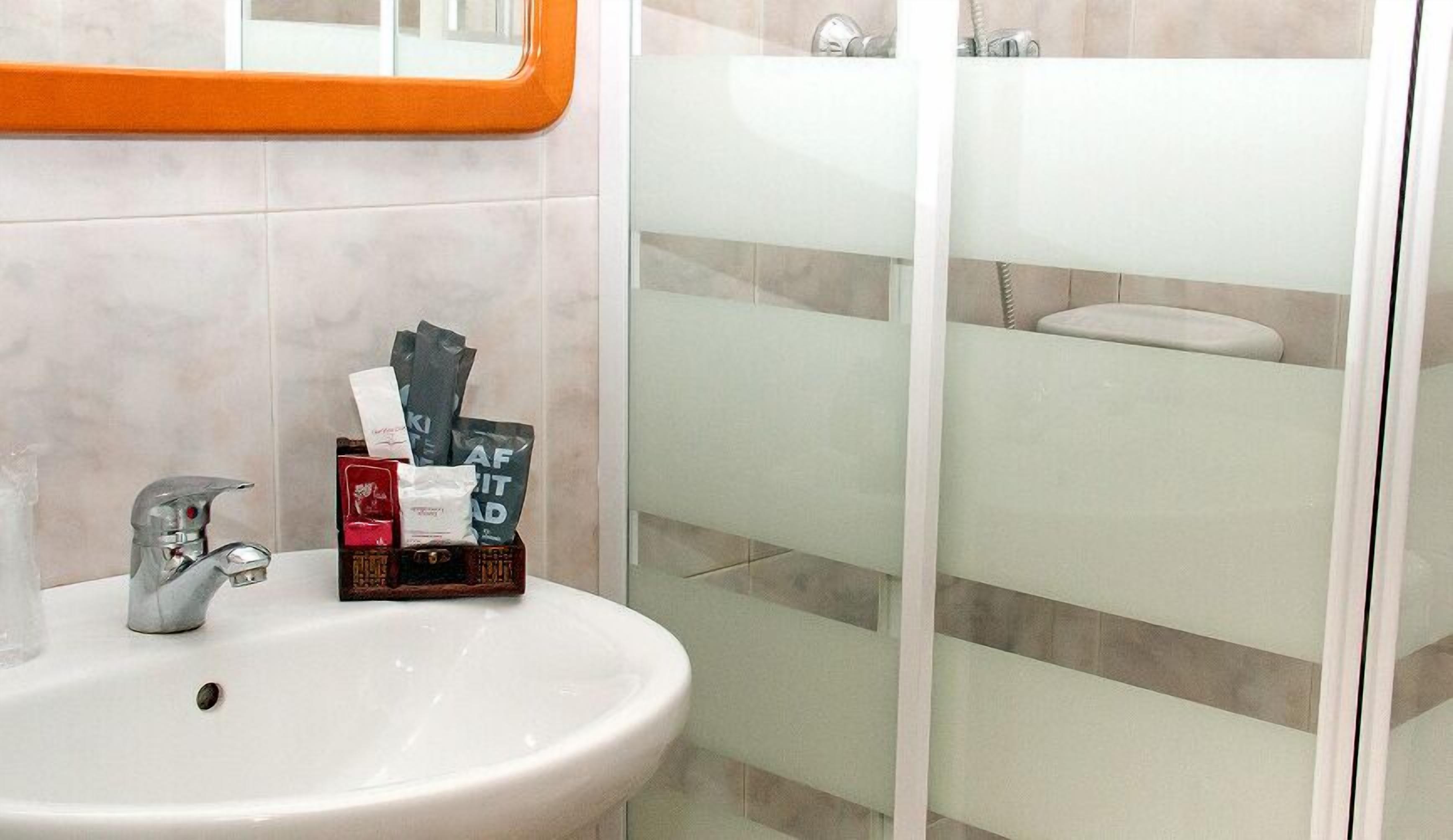 Un baño con lavamanos blanco, un espejo y zona de ducha.