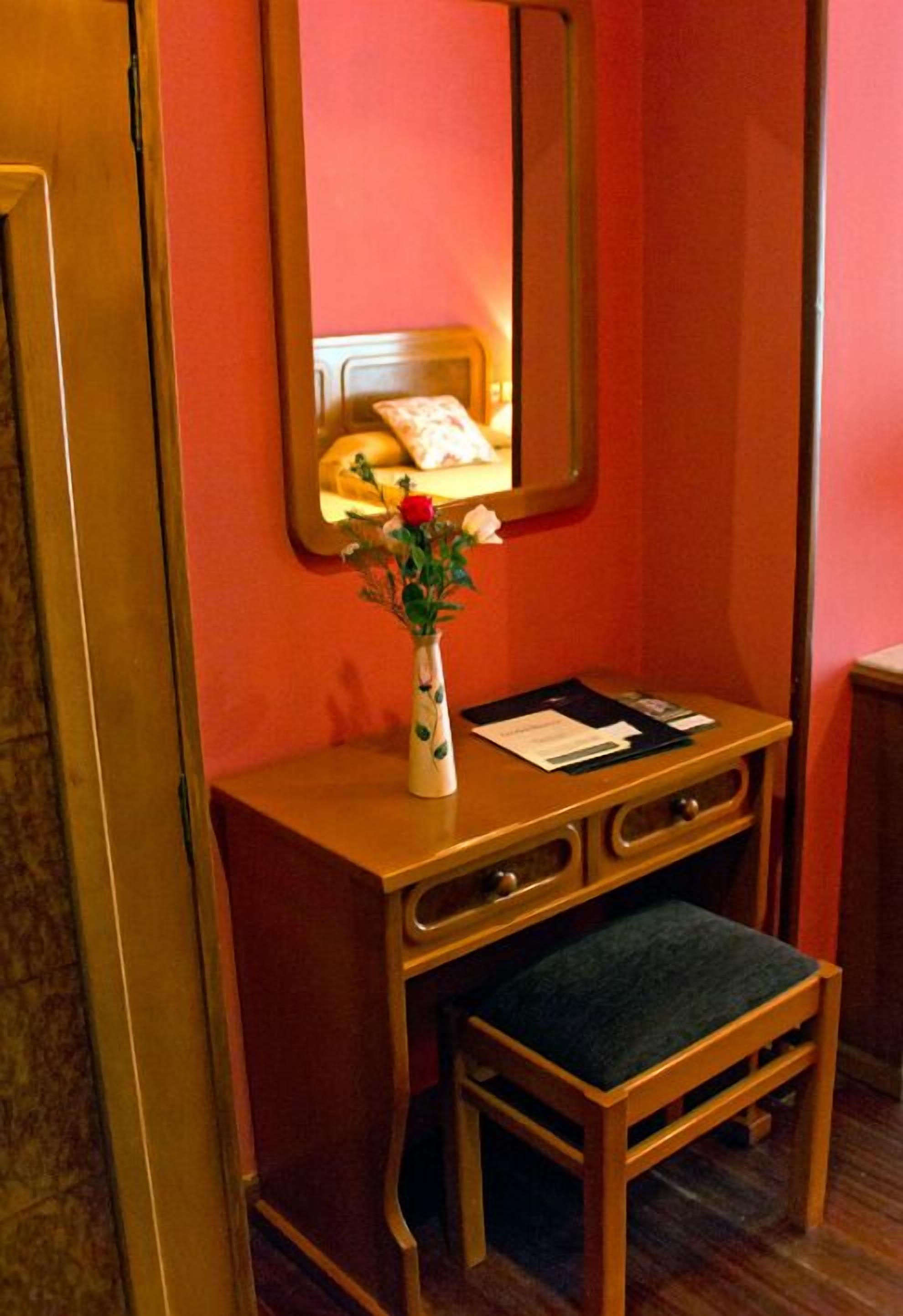 Een houten bureau met een bloemenvaas, een spiegel en een bank.
