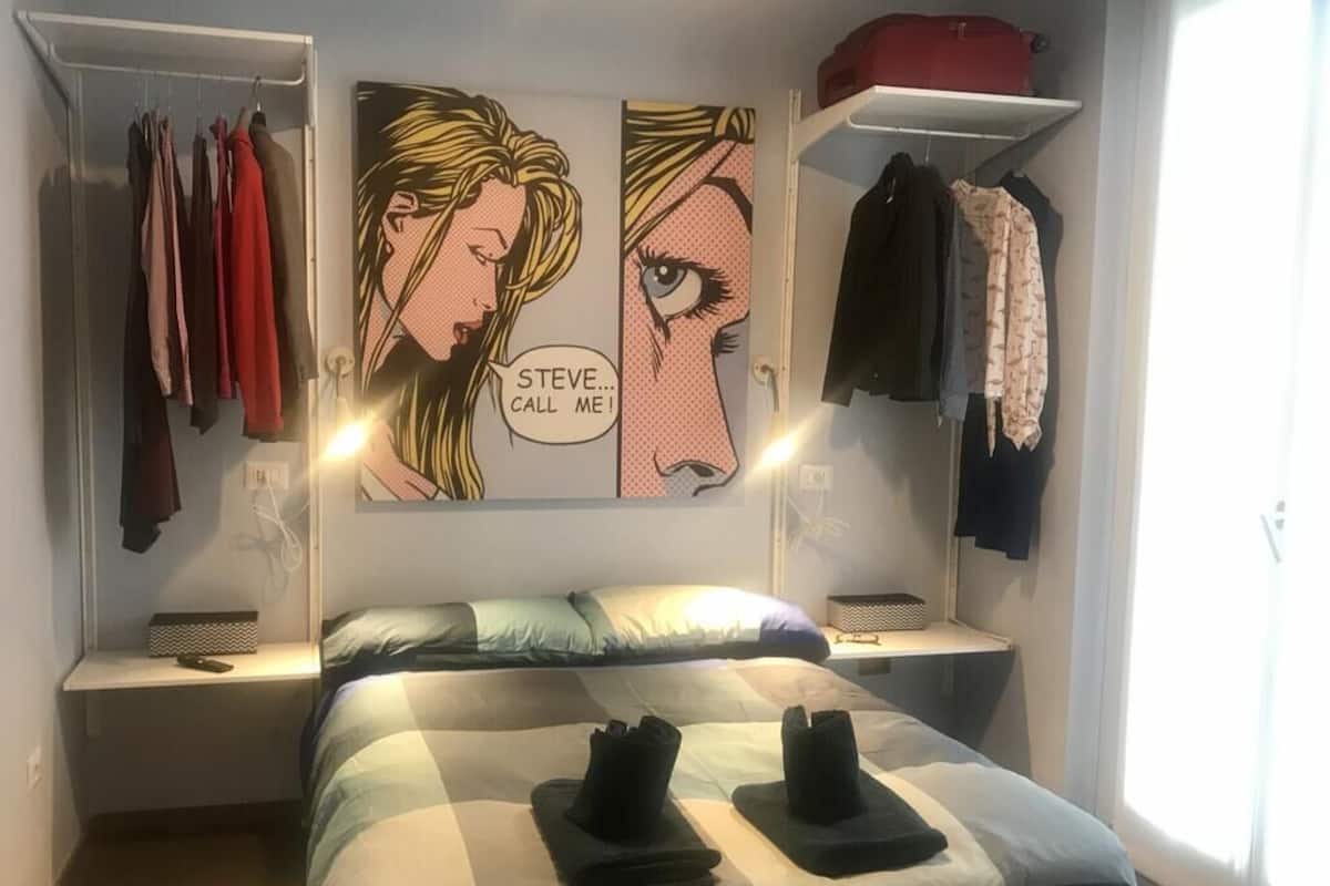 Un dormitorio con una cama, un armario con ropa colgada y una estantería con un bolso rojo.