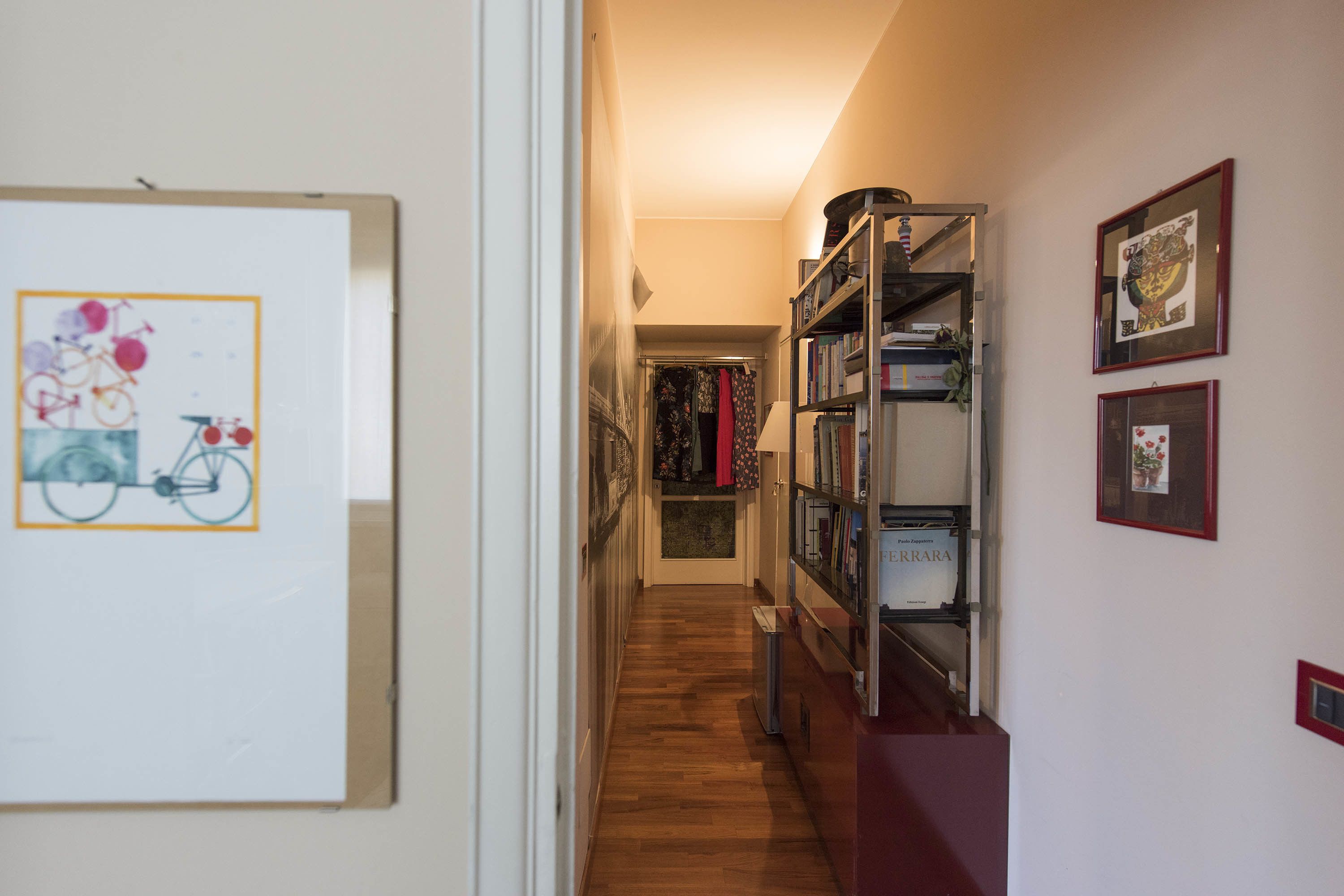 A narrow hallway with wooden flooring, a whiteboard with a bicycle illustration, and a bookshelf with various items.