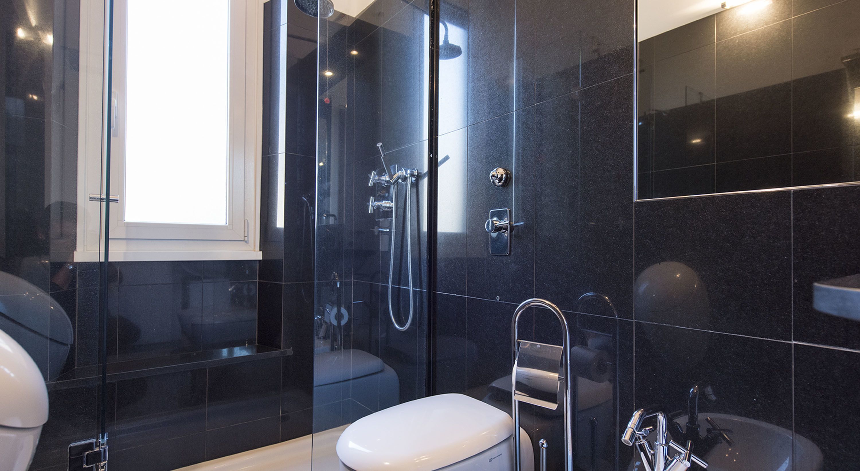 A modern bathroom with a glass-enclosed shower, a white toilet, and a sink with a chrome faucet.