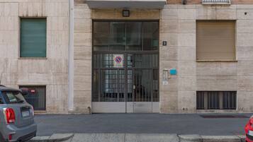 Entrada d'un edifici amb porta de vidre, reixa metàl·lica i un senyal de prohibició d'aparcament.