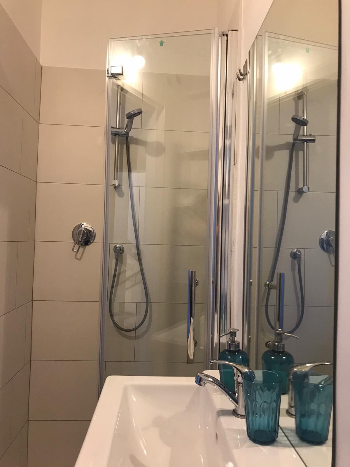 A modern bathroom with a glass-enclosed shower, a white sink, and blue glass cups on the counter.