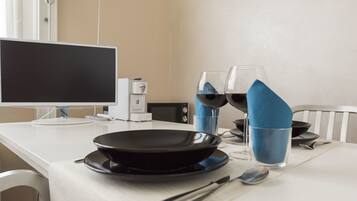 A dining table with a black plate, two wine glasses, a spoon, and a computer monitor.