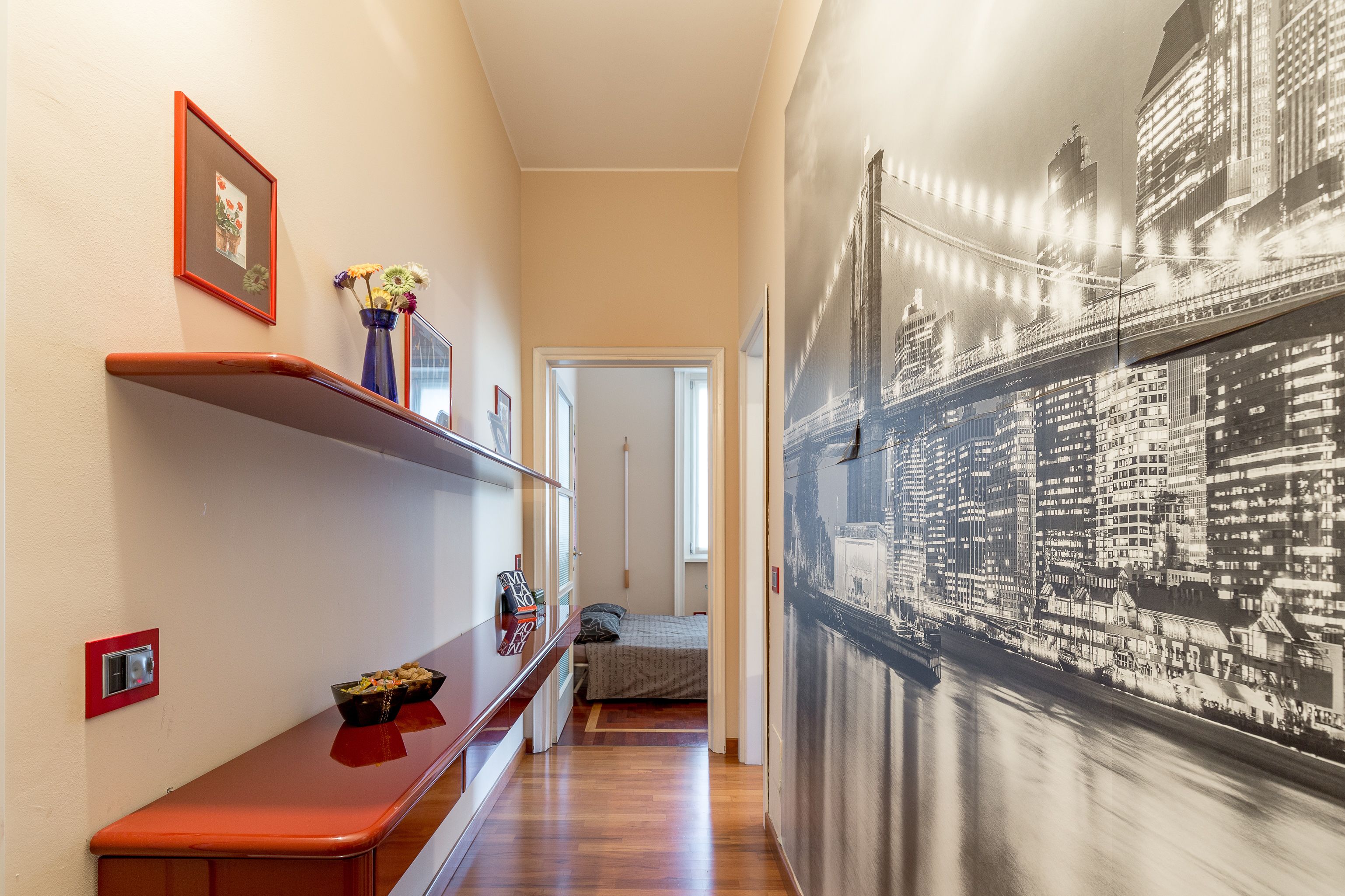 Ein Flur mit einer Holzbank, einem Blumenstrauß in einer Vase und einem gerahmten Bild an der Wand.