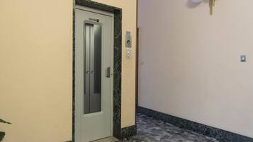 An elevator door with a marble frame, a wall-mounted light fixture, and a patterned floor.