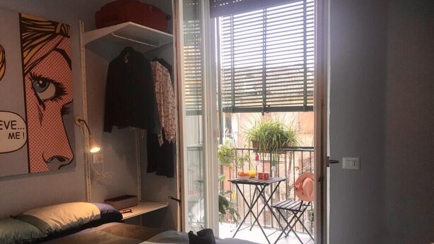 Et soveværelse med seng, bænk, bord og en balkon med bord og stole.