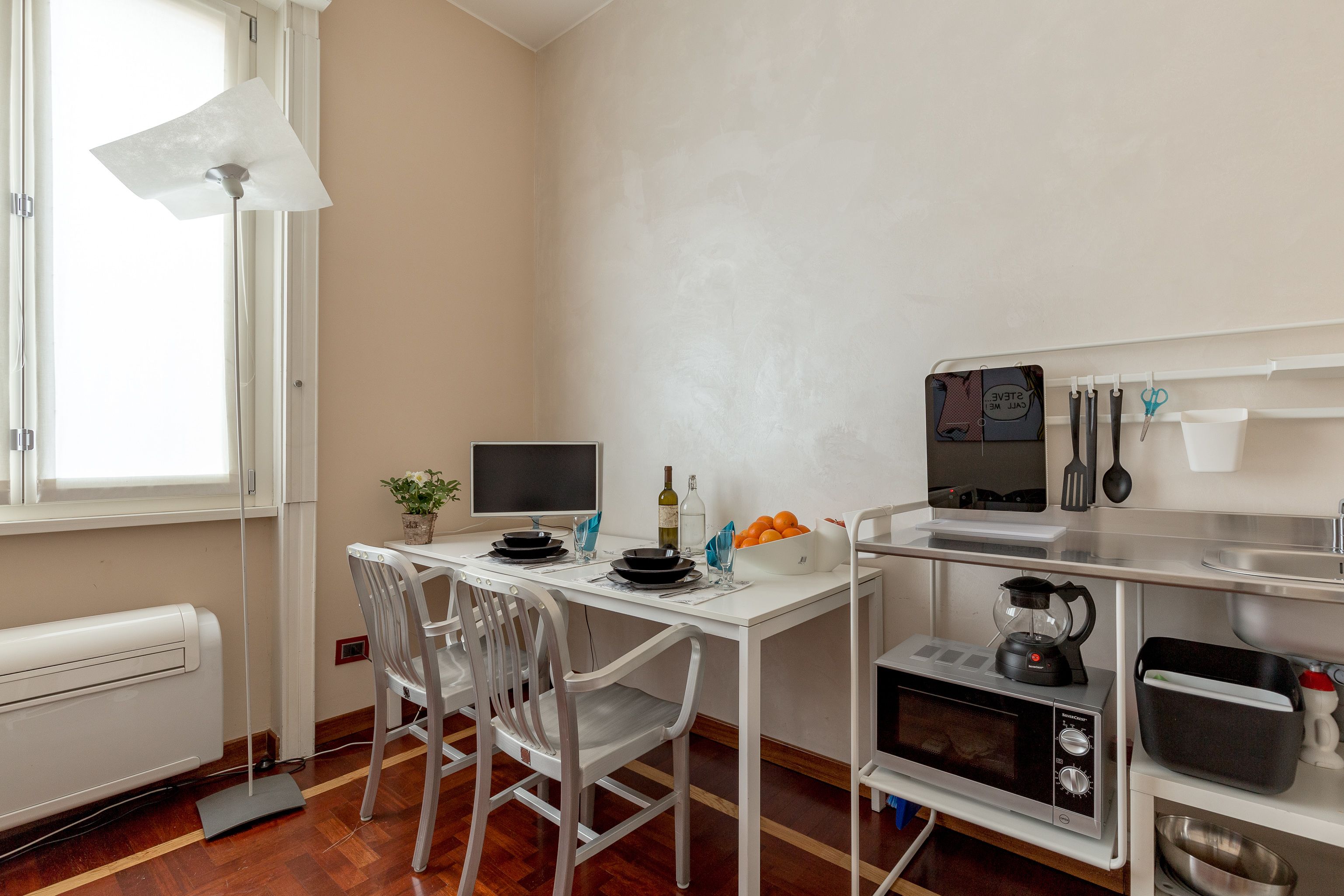 A compact kitchen with a white countertop, a microwave, a kettle, and a small refrigerator.