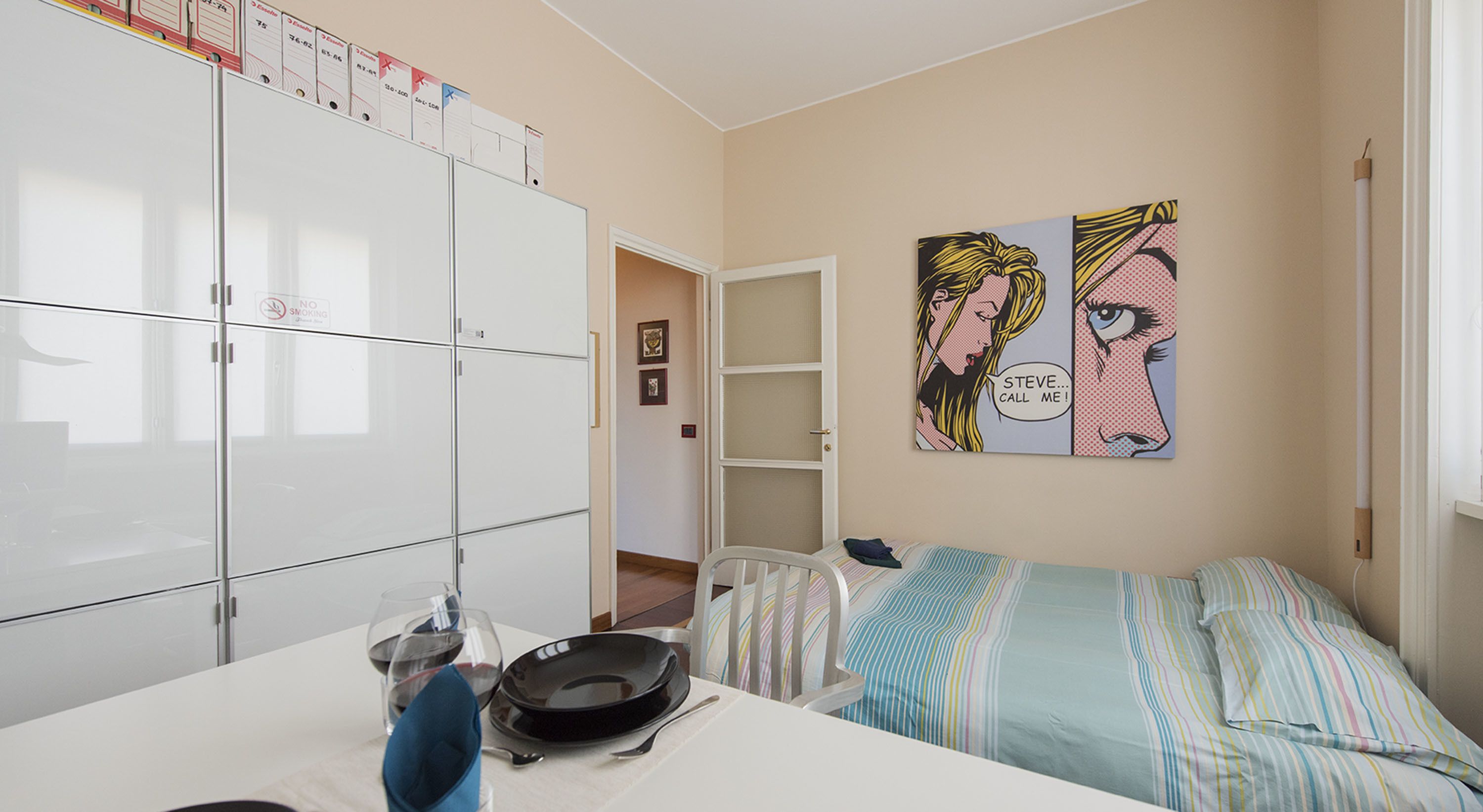 Une chambre à coucher avec un lit, une table à manger avec une assiette et un verre, et une armoire blanche.