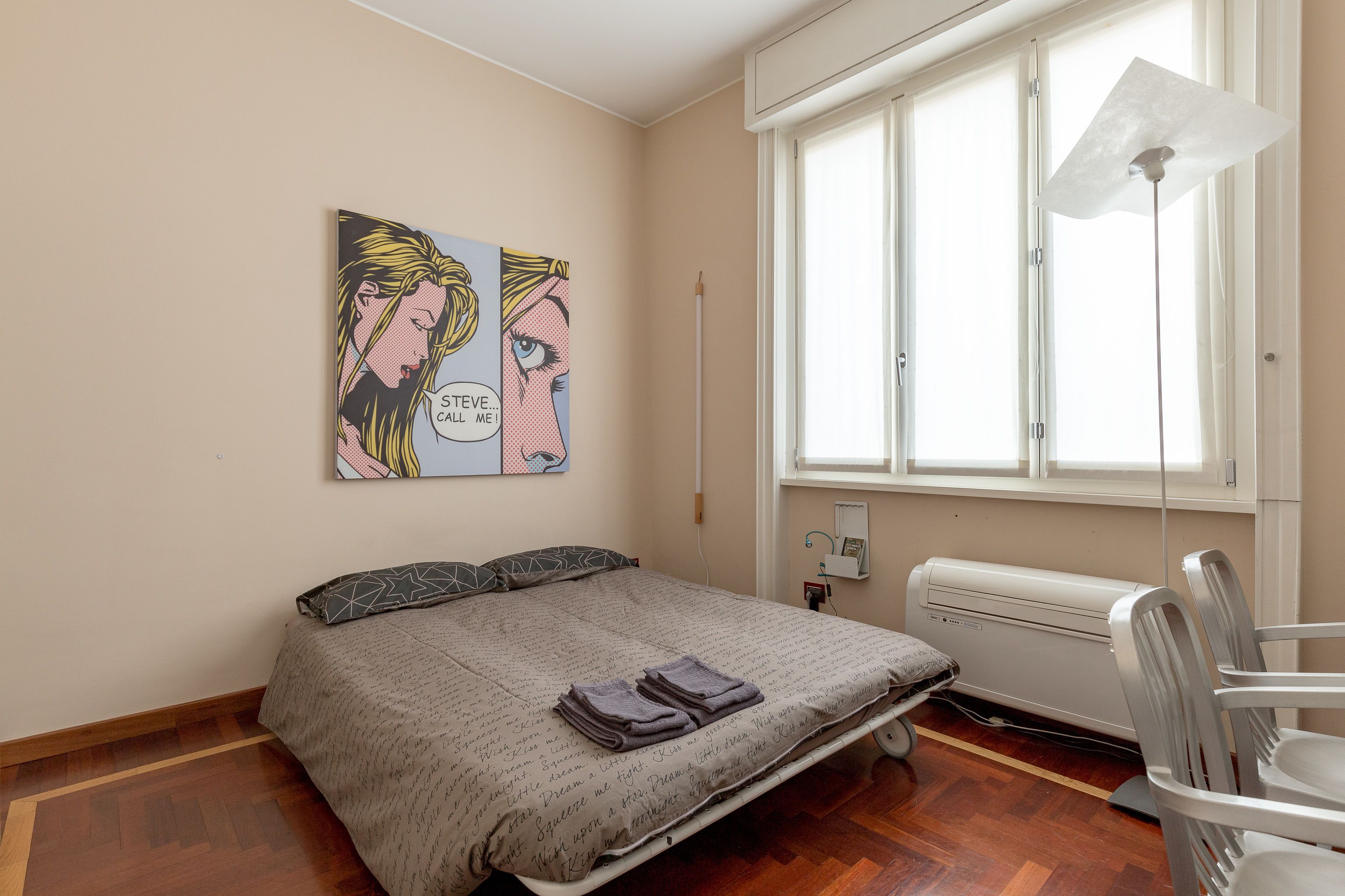 A bedroom with a bed, a radiator, a window, and a wall-mounted artwork.