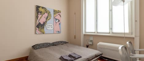 A bedroom with a bed, a radiator, a window, and a wall-mounted artwork.