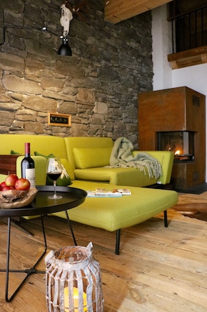 Ein gemütliches Wohnzimmer mit Steinwand, einem grünen Sofa, einem Kamin und einem Tisch mit einer Weinflasche und Äpfeln.