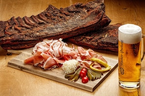 Ein Holzschnittbrett mit geschnittenem Fleisch, eingelegtem Gemüse und einem Glas Bier.