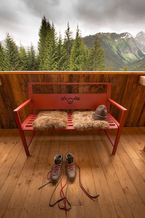 Eine Holzterrasse mit einer roten Bank, einem Fellteppich und einem Paar schnürbare Stiefel.