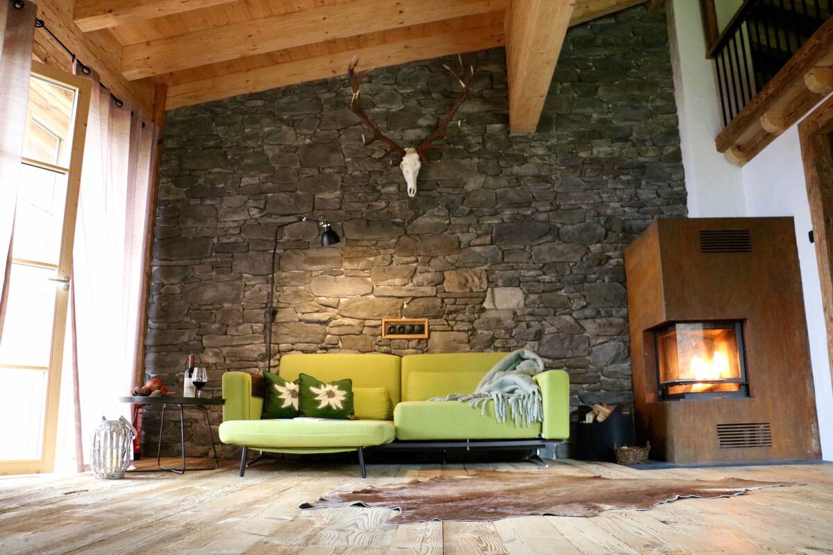 Un salon chaleureux avec un mur en pierre, un canapé vert, une cheminée et un crâne de cerf accroché au mur.