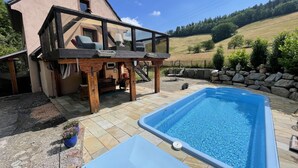 Un patio trasero con piscina, terraza de madera y pared de piedra.