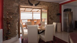 Comedor con pared de piedra, una araña y vistas a un espacio exterior a través de un vidrio.