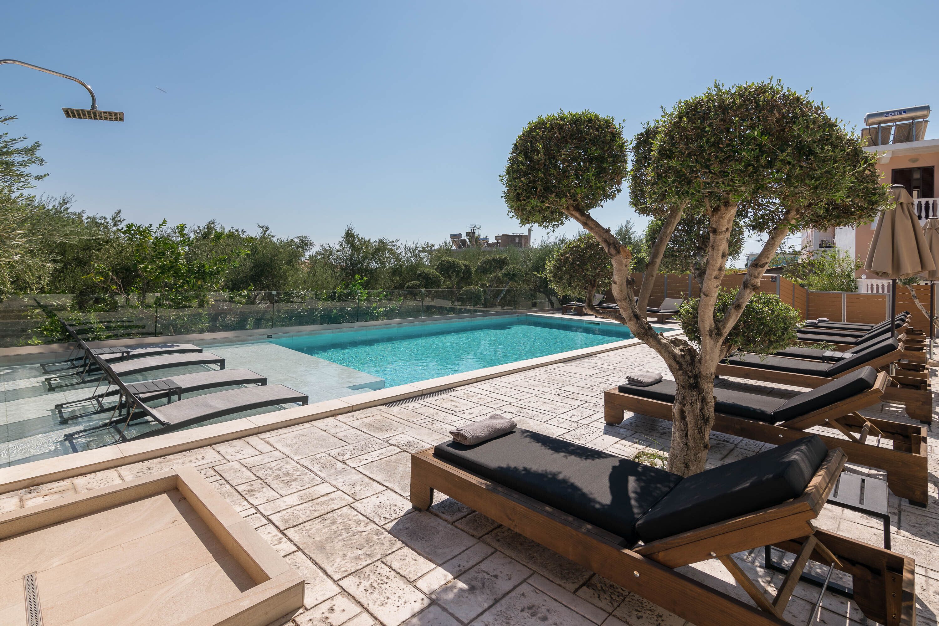 Un área de piscina en la azotea con sillones de descanso y un árbol.