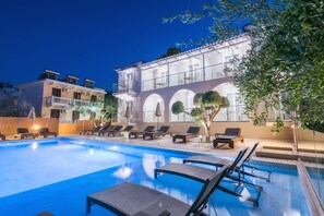 A swimming pool with lounge chairs and a building with arched windows and balconies. - Litore Luxury Living (Zakynthos)
