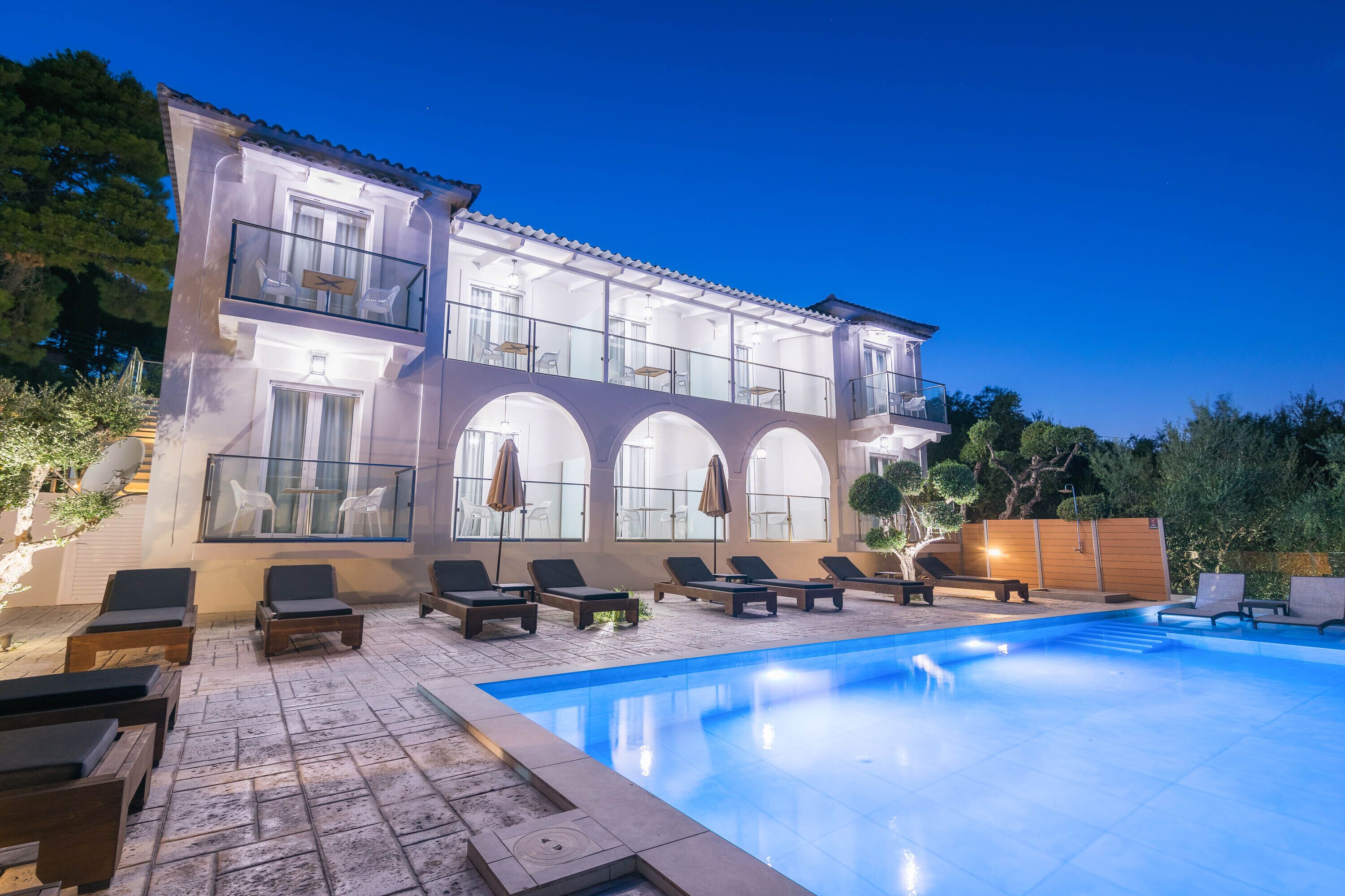 A modern building with a swimming pool, outdoor seating, and a balcony with glass railings.