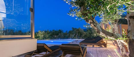 A rooftop pool area with wooden lounge chairs and a glass balustrade overlooking a swimming pool.