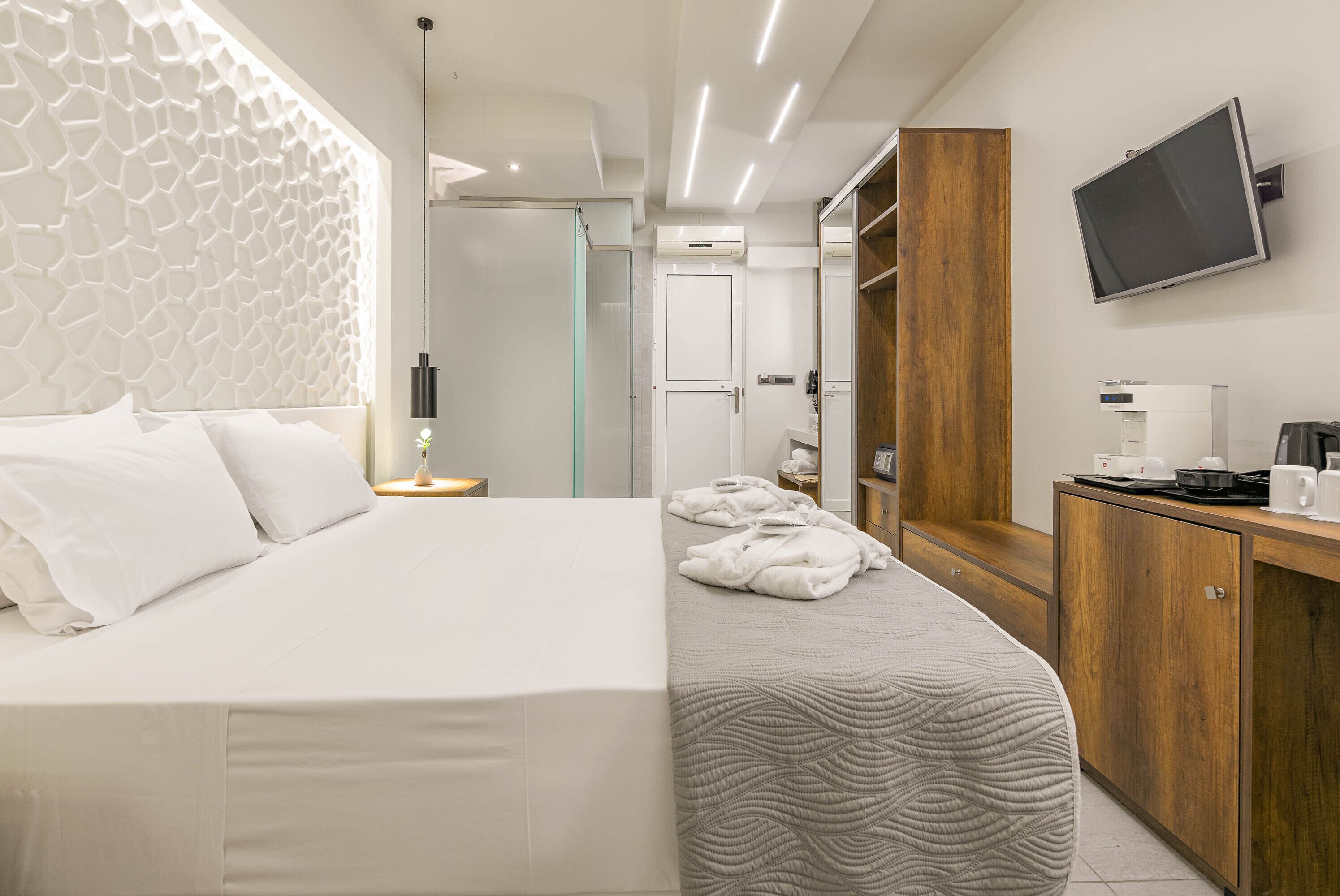 Camera d'albergo moderna con un letto grande, un comodino con lampada, un armadio in legno, una televisione e un bagno con box doccia in vetro.