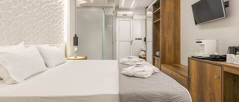 Camera d'albergo moderna con un letto grande, un comodino con lampada, un armadio in legno, una televisione e un bagno con box doccia in vetro.