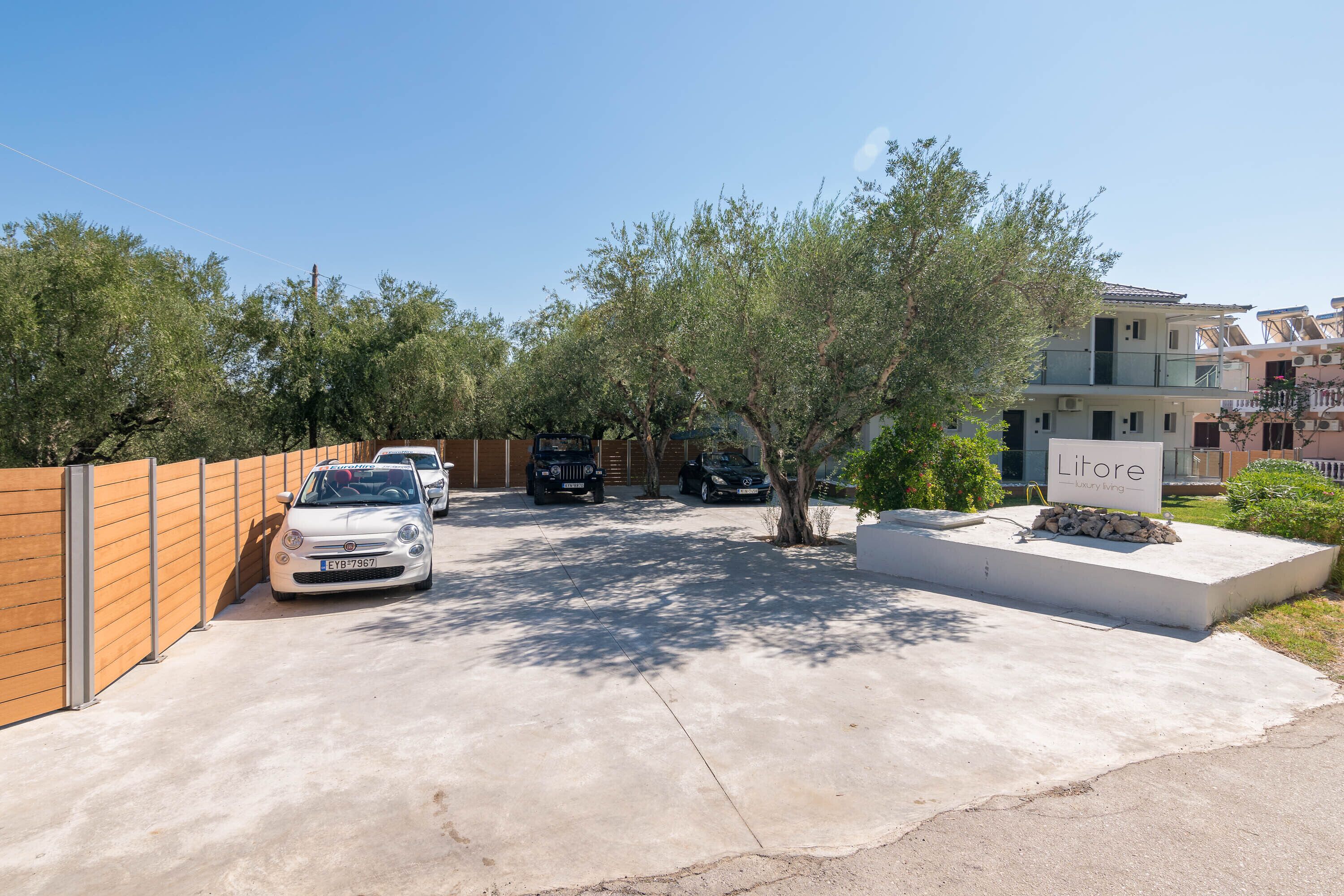 Una zona residenziale con auto parcheggiate, un cartello con la scritta 'Litore Luxury Living' e un vialetto in cemento.