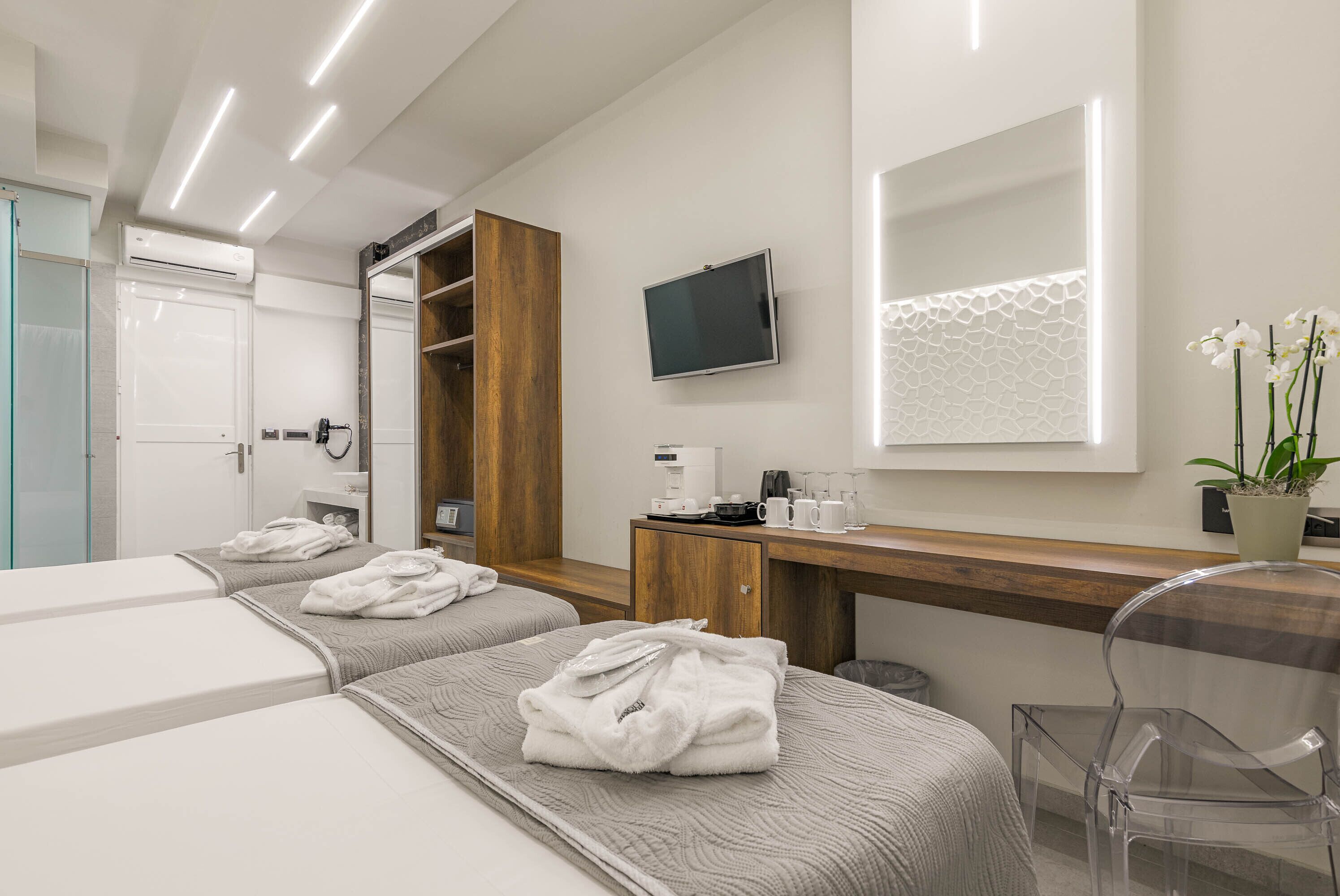 A modern hotel room with two beds, a wooden desk, a TV, and a mirror.