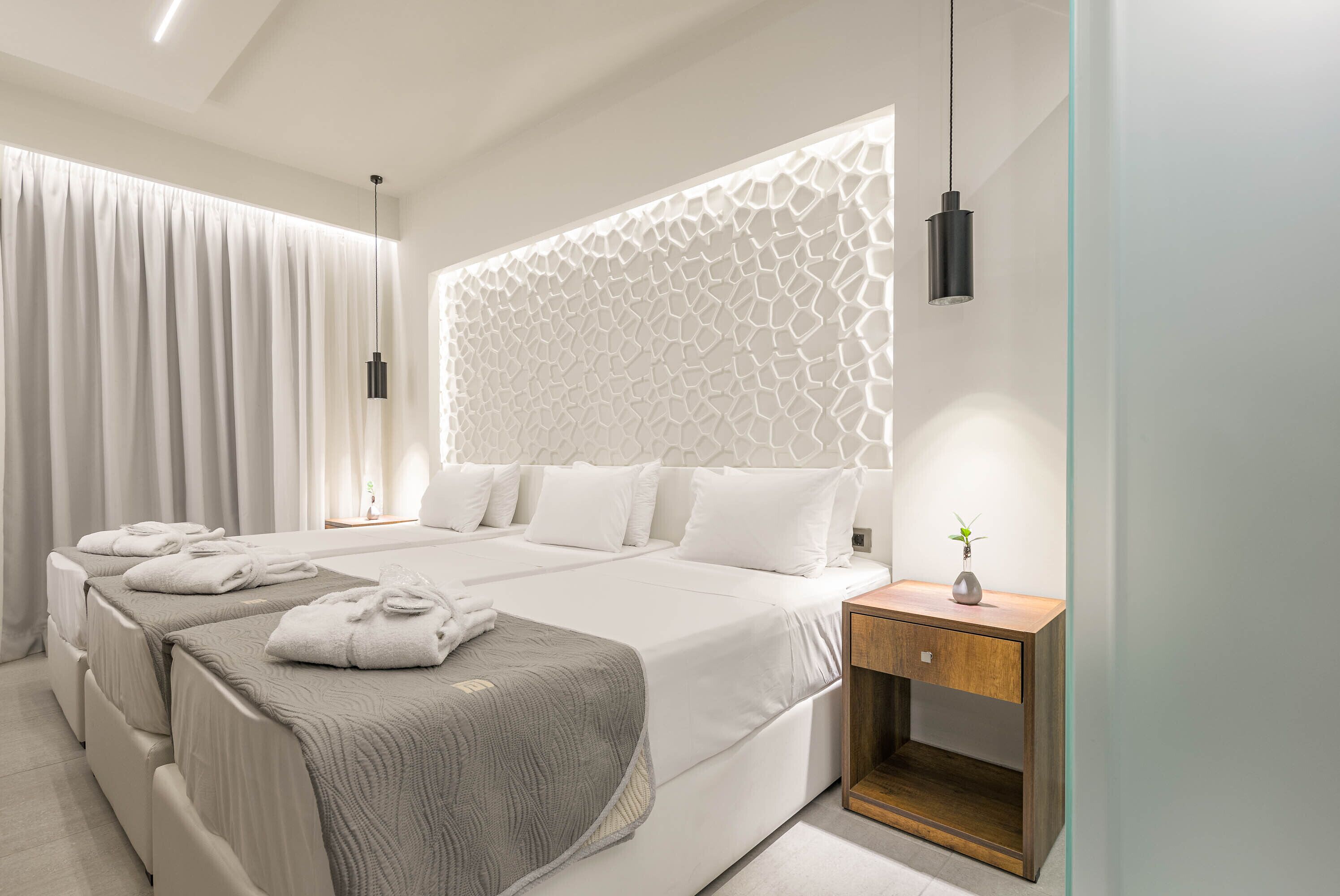 A modern hotel room with a large bed, a bedside table with a vase, and a decorative wall panel.