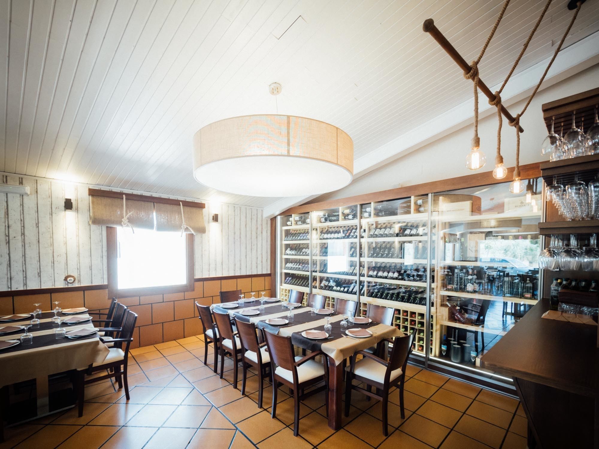 En restaurang med ett långt bord, stolar och ett vinställ fullt med flaskor.