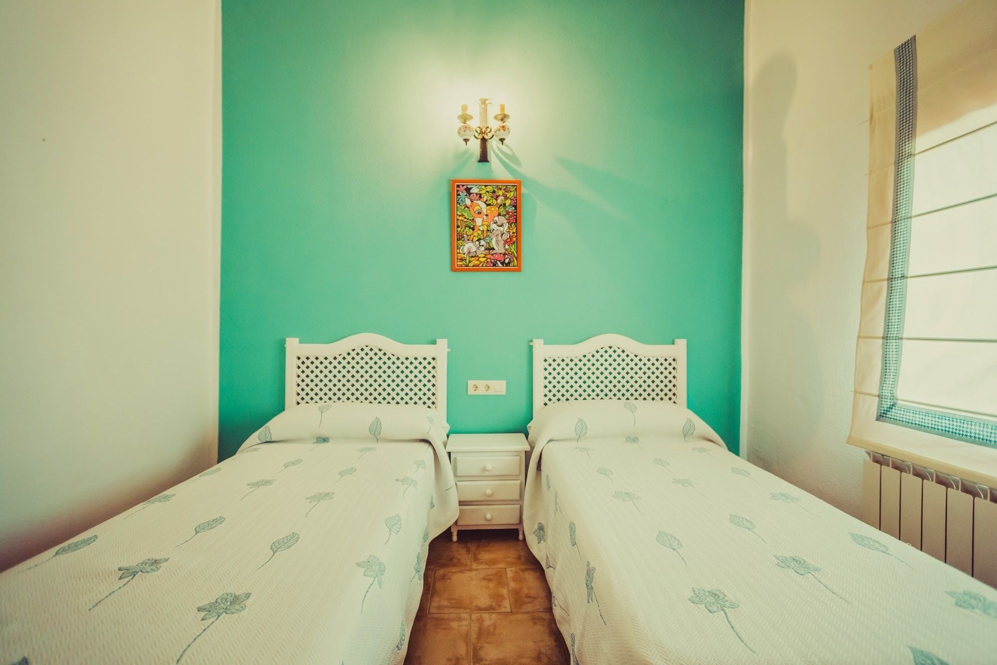 Una habitación pequeña con dos camas individuales, una lámpara de pared y una ventana con vistas.