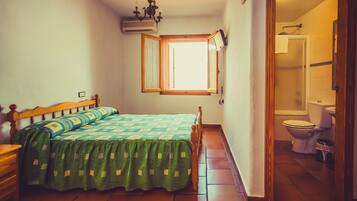 Un dormitorio pequeño y bien iluminado con una cama individual, un aparador de madera y una ventana con contraventanas abiertas.